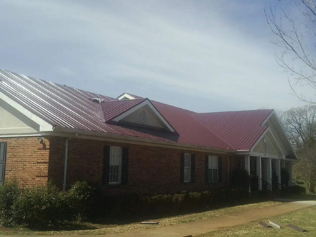 Red metal roof with gabled entries on a long brick building, from a Hail Damage Roof Repair job in Depoe Bay