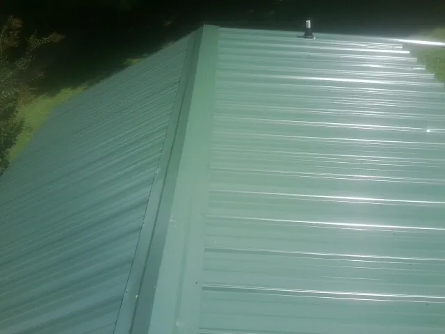 New green metal panels meeting at the ridge of a roof — Flat Roof Repair work by our crew in Depoe Bay