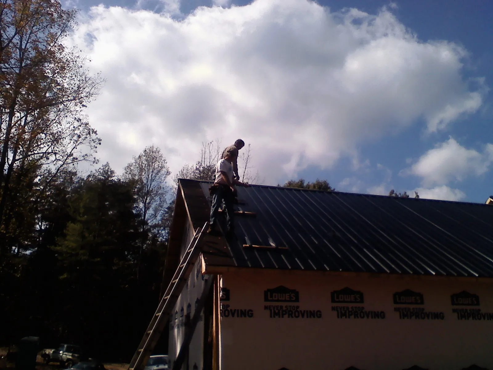 Roofer fastening dark metal panels high against a cloudy sky, from a Roof Inspection job in Depoe Bay