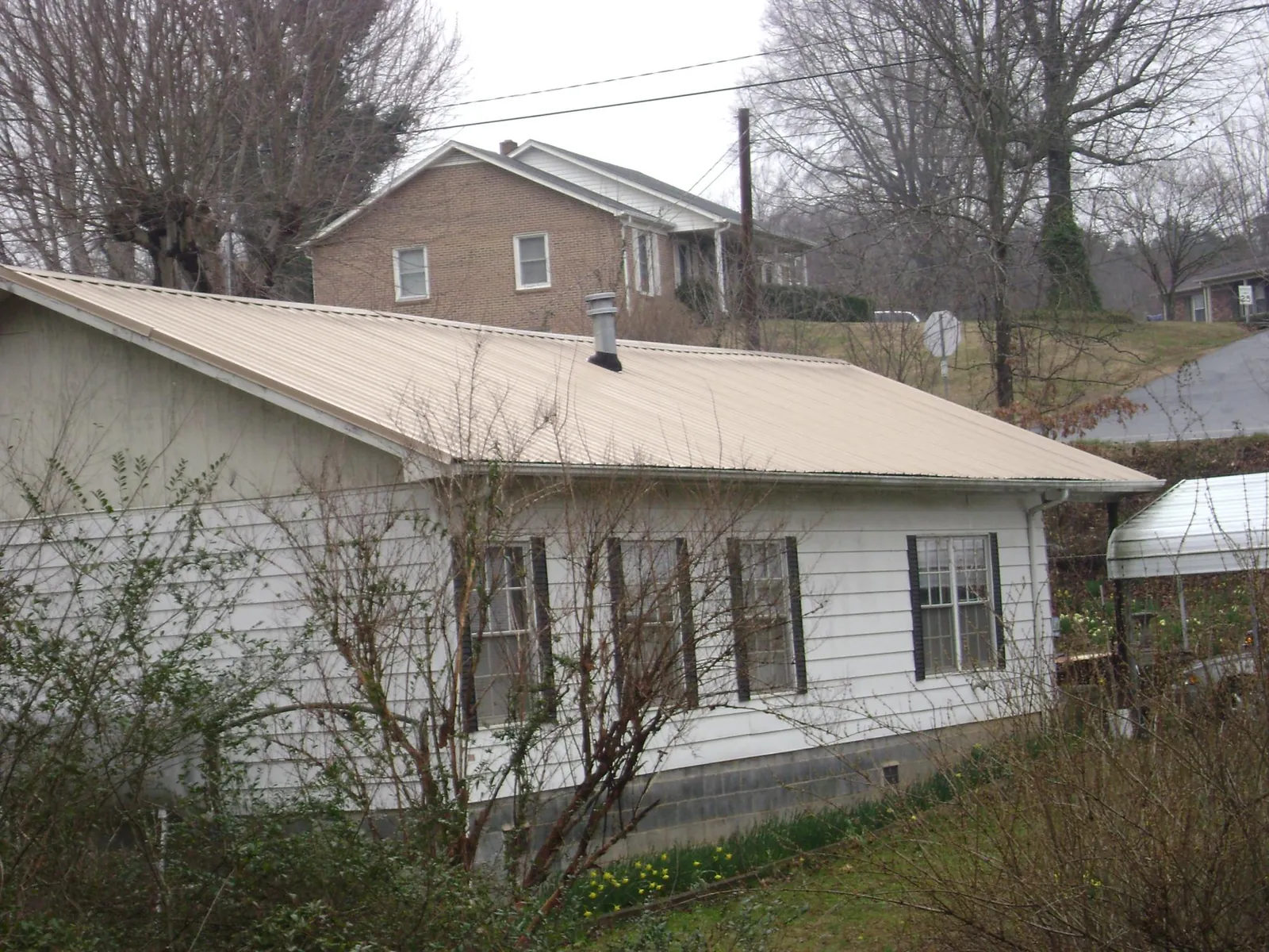 Tan metal roof on a white sided house set into a hillside — Commercial Roofing by Roofing Brothers in Depoe Bay
